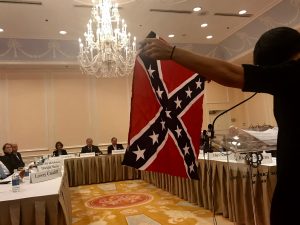 Heather Redding, who is married to a UNC graduate, holds up a confederate flag to the Board of Trustees while voicing her opposition to Silent Sam. (Rachel Bridges/Carolina Connection)
