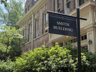 A black sign outside of a building and bushes that reads "SMITH BUILDING"