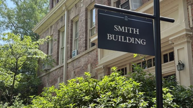 A black sign outside of a building and bushes that reads "SMITH BUILDING"