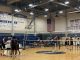 High School male boys' volleyball players in uniforms on both sides of a volleyball net in a high school gym.